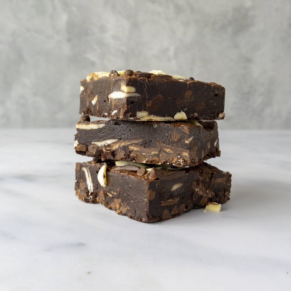 Stack of chocolate brownies with milk, dark and white chocolate on a marble surface