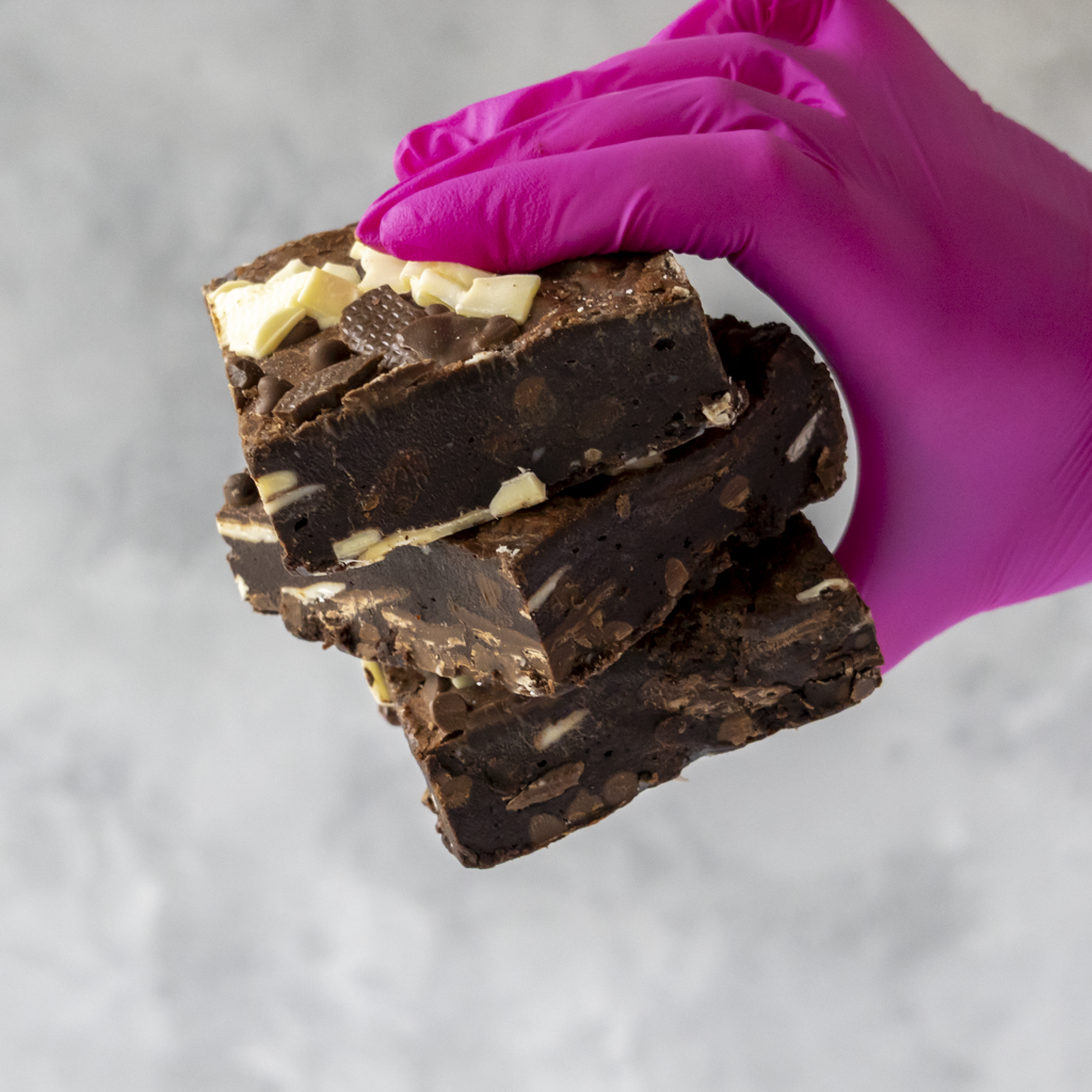Stack of chocolate brownies held by a hand wearing a pink glove on a gray background