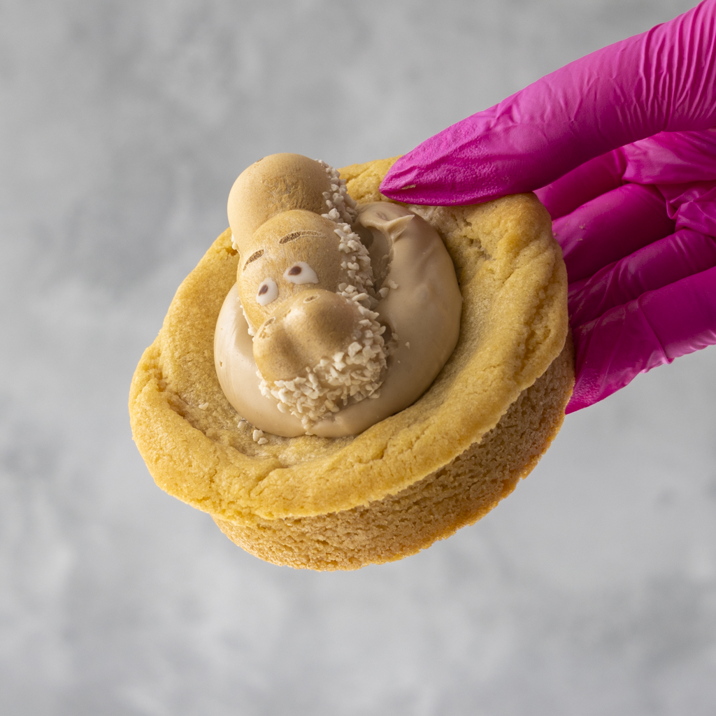 White Bueno Hippo Deluxe Cookie with a cream filling held by a hand wearing a pink glove on a gray background