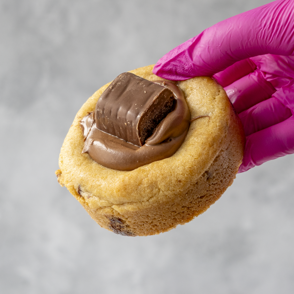 Cadbury Wispa Deluxe Cookie with chocolate filling held by a hand wearing a pink glove on a gray background