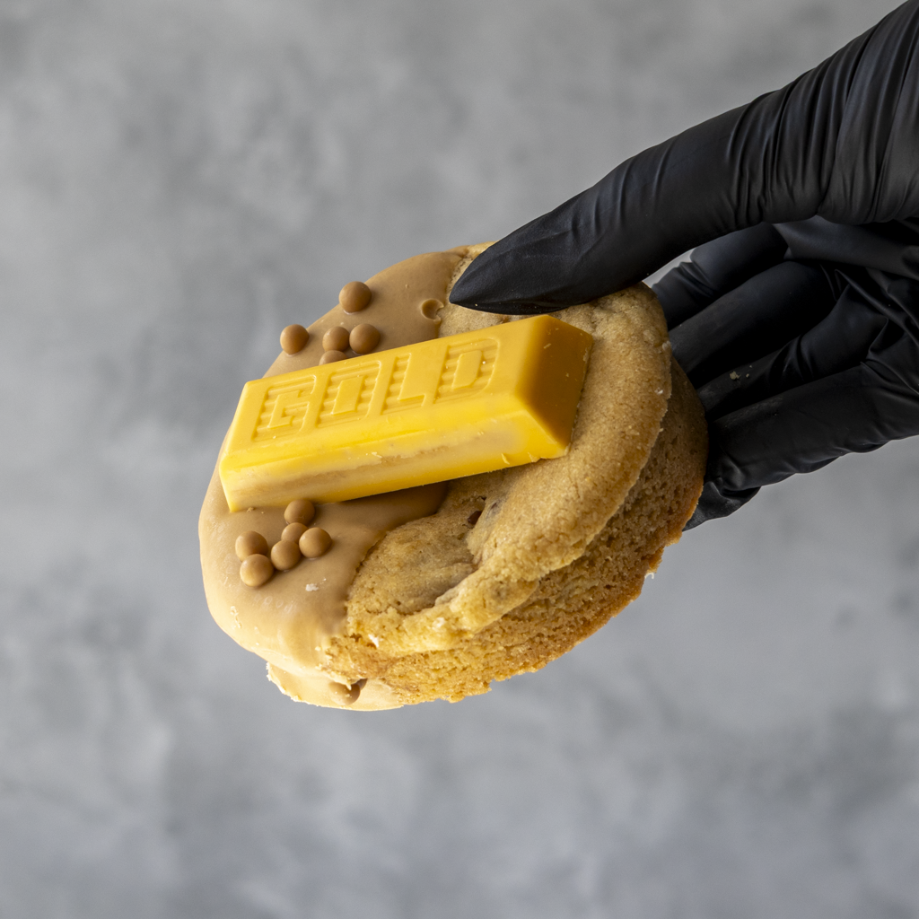 Gold Bar Deluxe Cookie by DoughGirl, with a GOLD chocolate bar on top, holding by a black gloved hand