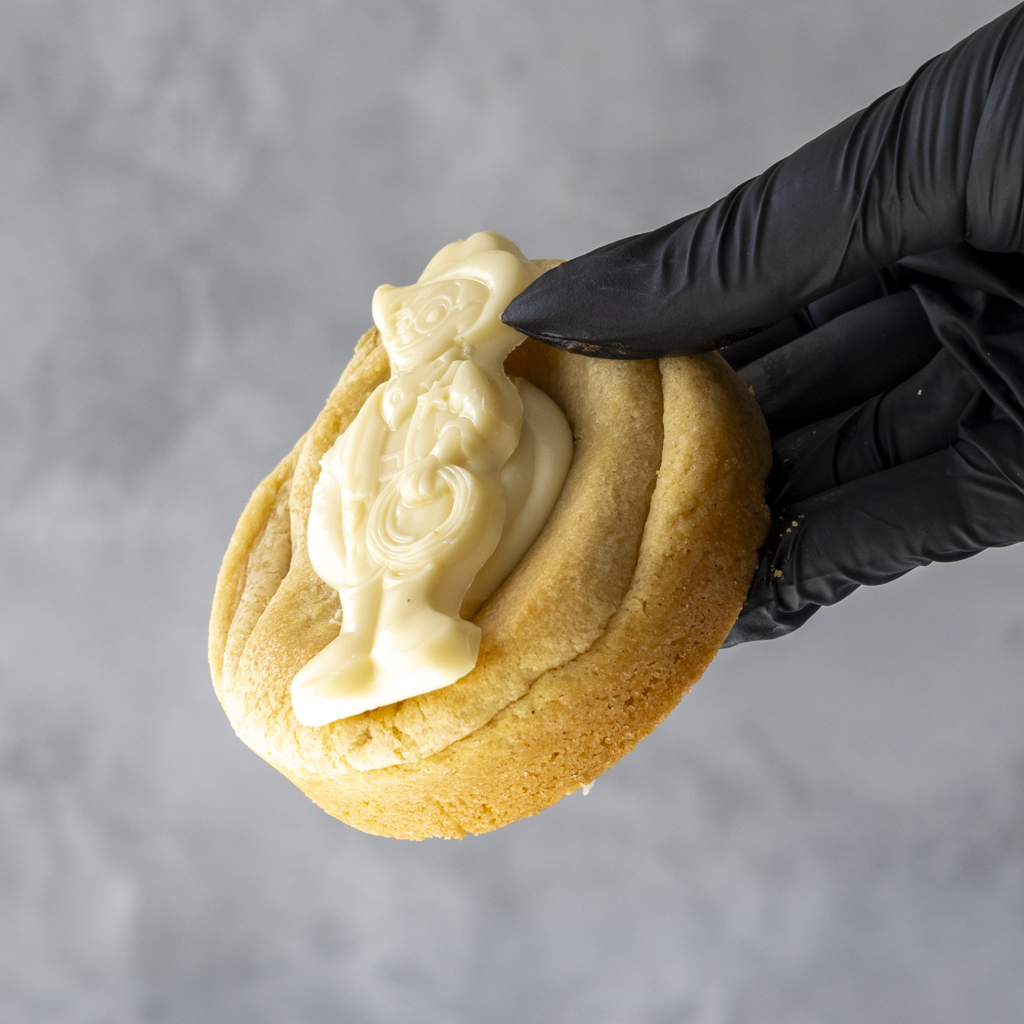 Milkybar Bliss Deluxe Cookie with cream filling held by a black gloved hand against a gray background