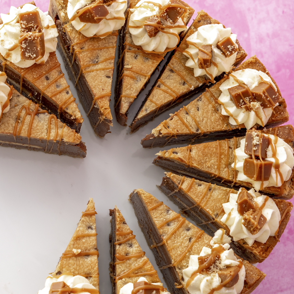 Triangular slices of a Banoffee Cookie Pie with chocolate, caramel, and whipped cream on a pink background.