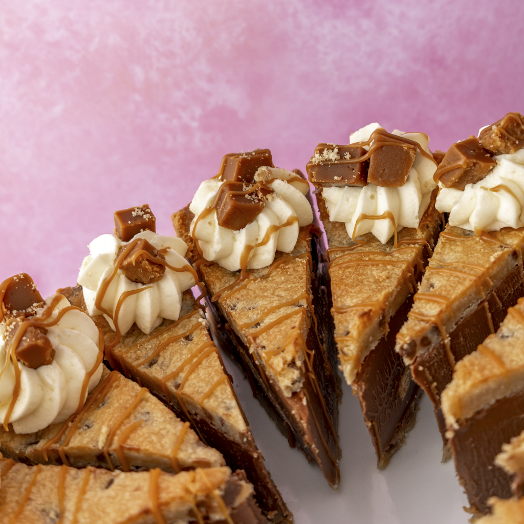 Close-up of Banoffee Cookie Pie Slices with white cream and banoffee chunks on a white plate against a pink background