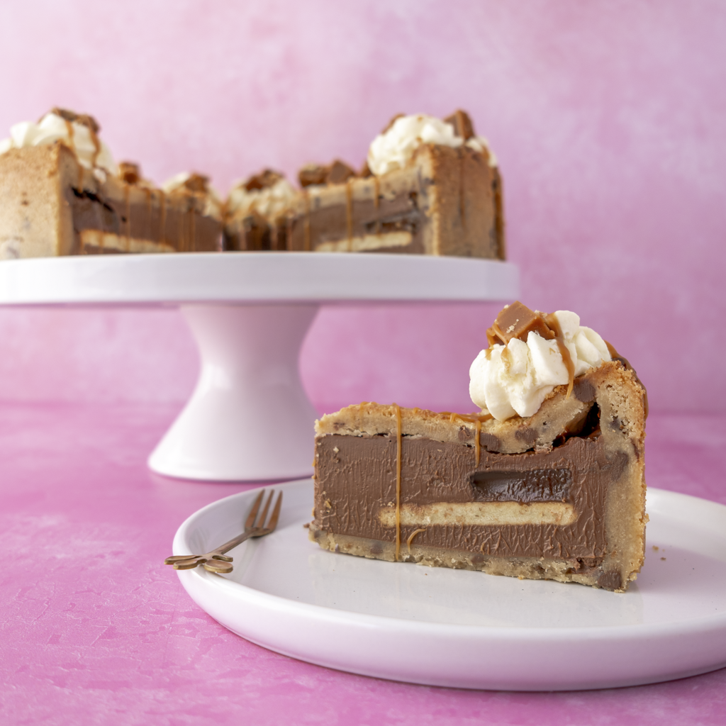 Slice of layered chocolate cake with white cream on a white plate against a pink background