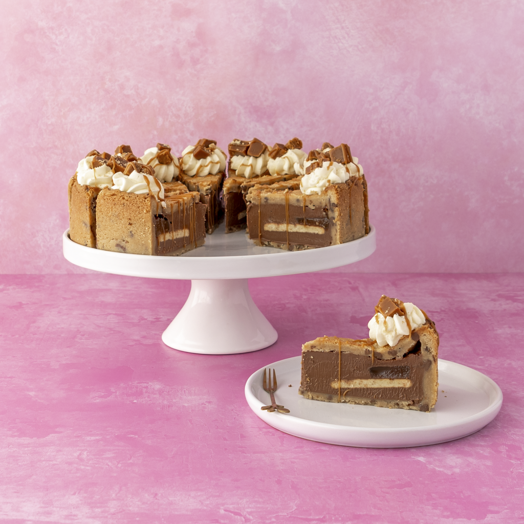 Full Banoffee Cookie Pie with layers on a white cake stand and plate against a pink background