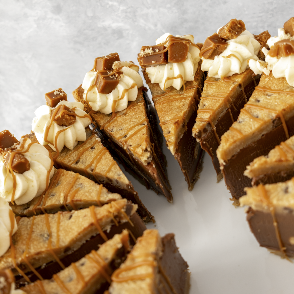 Slices of DoughGirl Banoffee Cookie Pie with white cream and caramel drizzle cut into slices on a light background