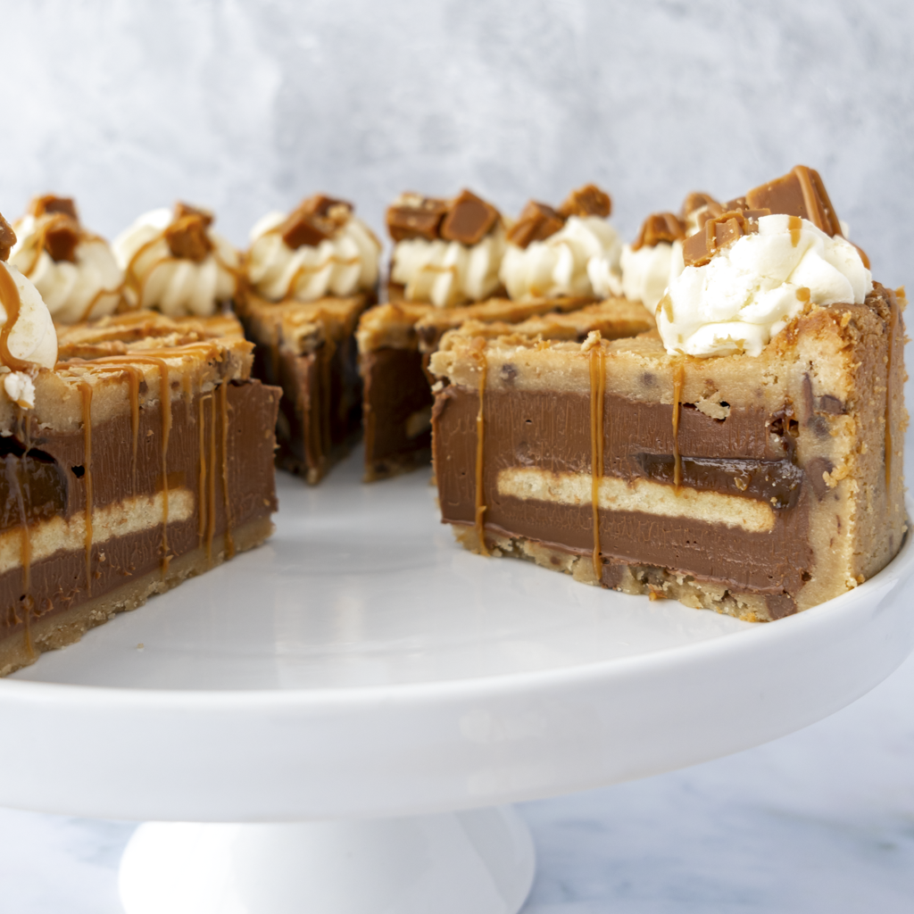 Layered chocolate and caramel dessert on a white cake stand with a marble background