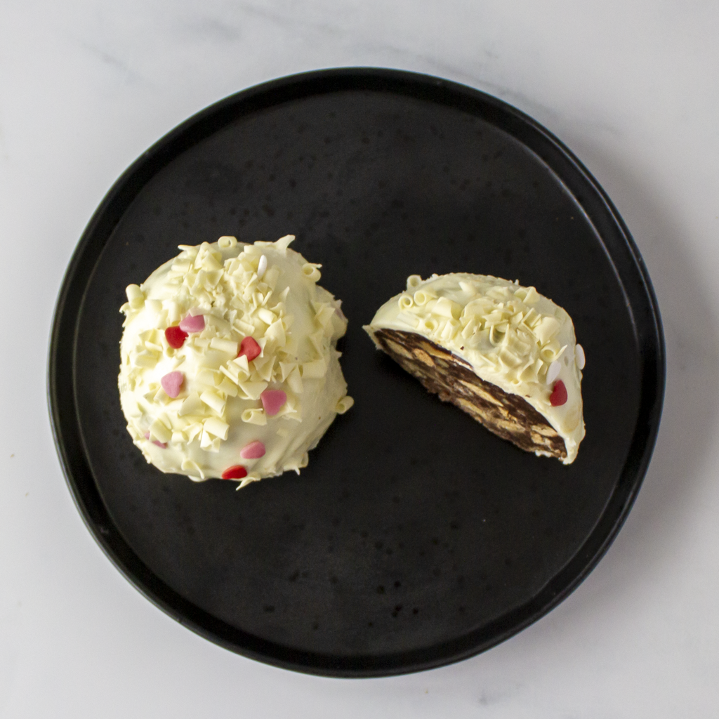 Two Filthy Fluff Brookie Choccy Boom Bites on a black plate with white frosting and colorful sprinkles.