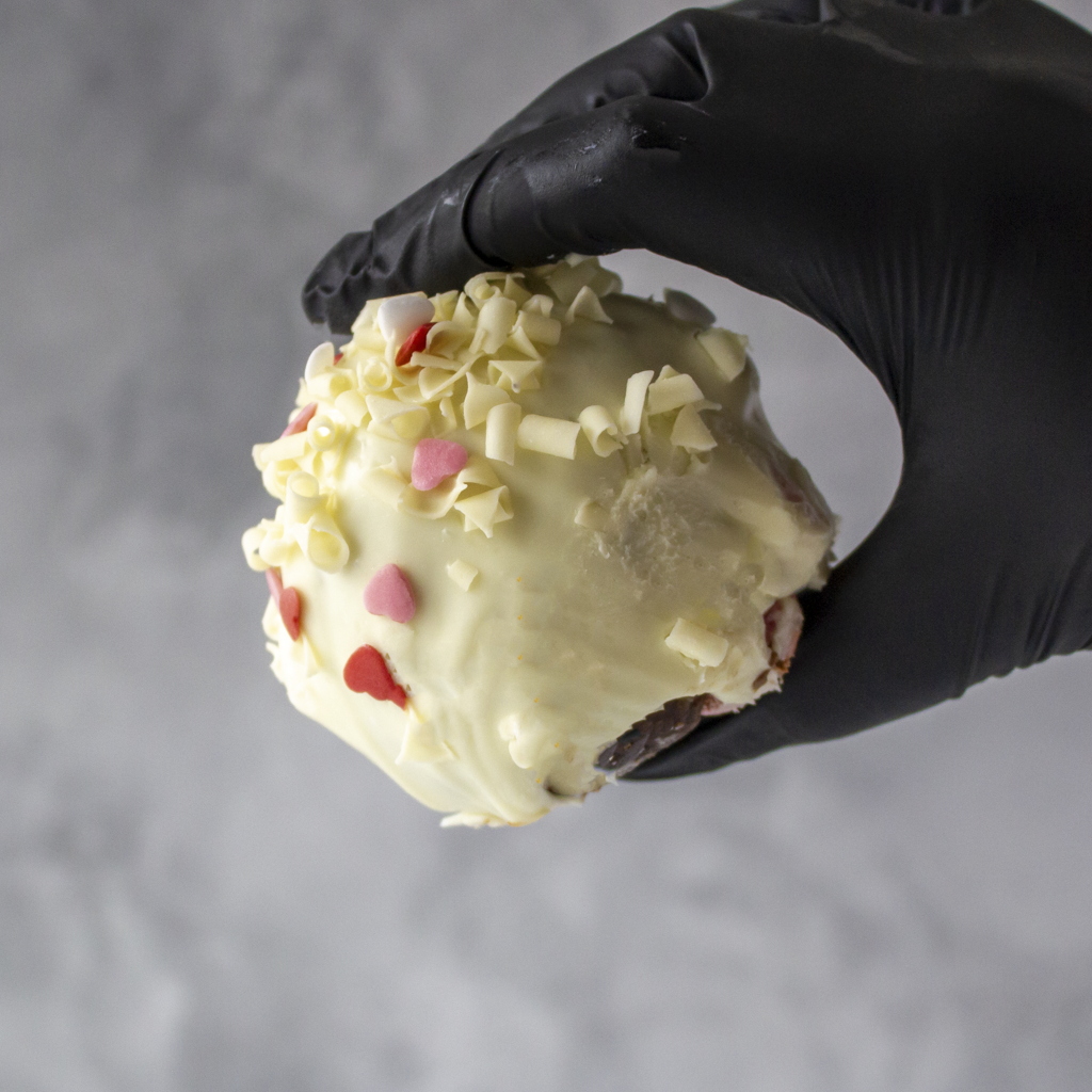 Hand wearing a black glove holding a Filthy Fluff Brookie Choccy Boom Bites dessert against a gray background