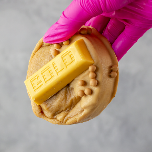 Gold Bar Deluxe Cookie with a chocolate bar imprint held by a gloved hand on a gray background