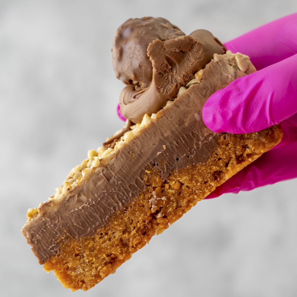 Close-up of a DoughGirl Hazelnut Cornflake Pie Slice with a hand wearing pink gloves holding it.