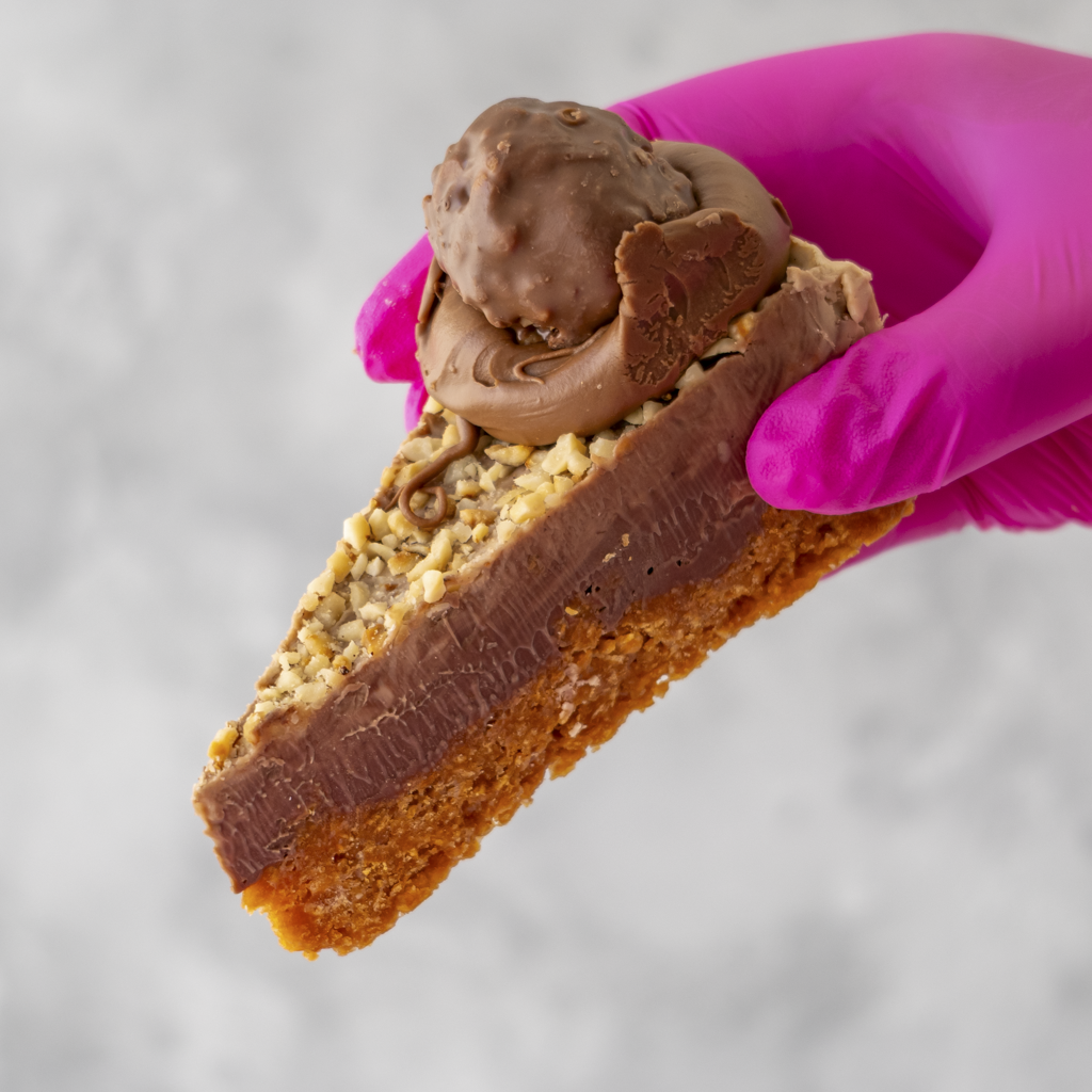 Hazelnut Cornflake Pie Slice held by a hand wearing a pink glove on a gray background