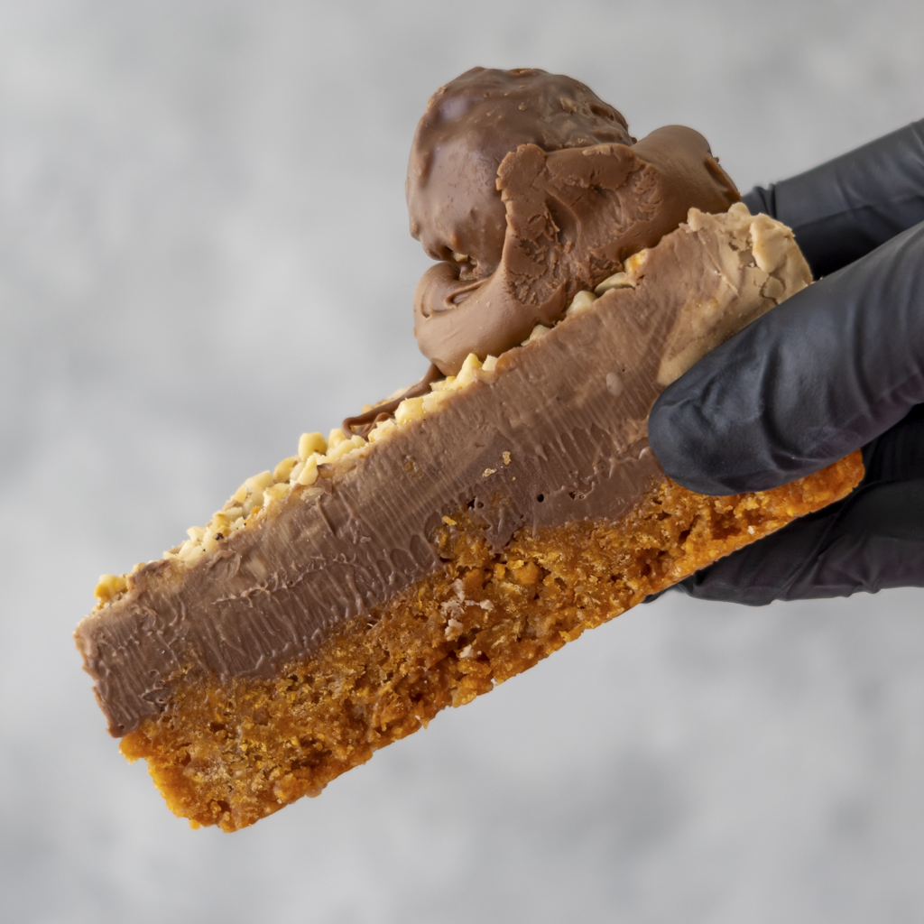 Hazelnut Cornflake Pie Slice with a person wearing black gloves holding it against a neutral background