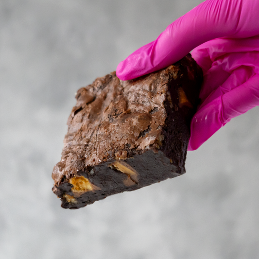 DoughGirl Honeycomb Crunch Brownie Slab held by a hand wearing a pink glove against a neutral background