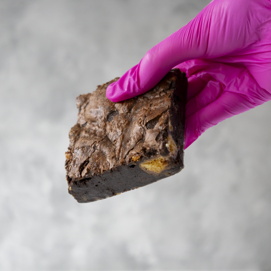 Hand wearing a pink glove holding a Honeycomb Crunch Brownie Slab with a blurred background