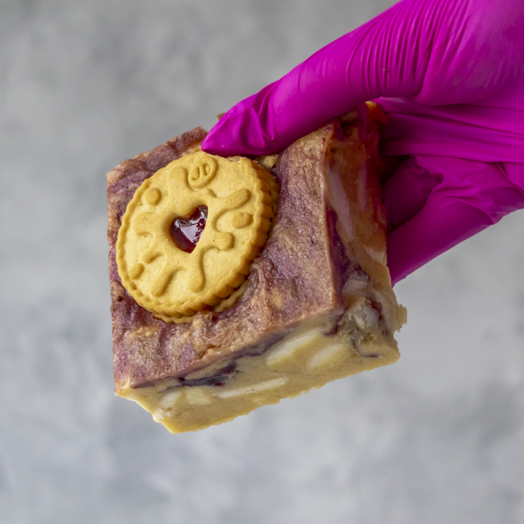 Hand holding a piece of Jammie Dodger Blondie Slab against a neutral background