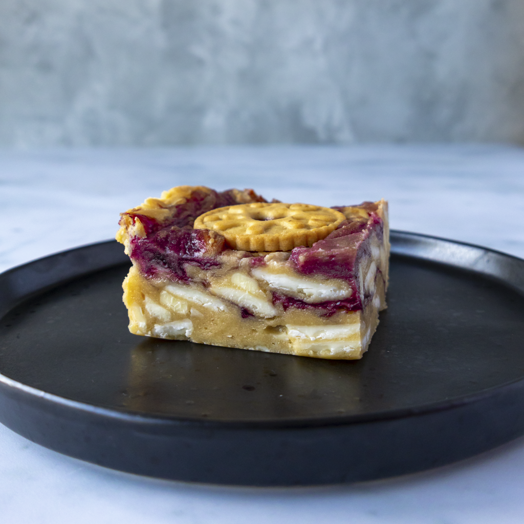 Slice of Jammie Dodger Blondie Slab with white chocolate chunks on a black plate with a gray background