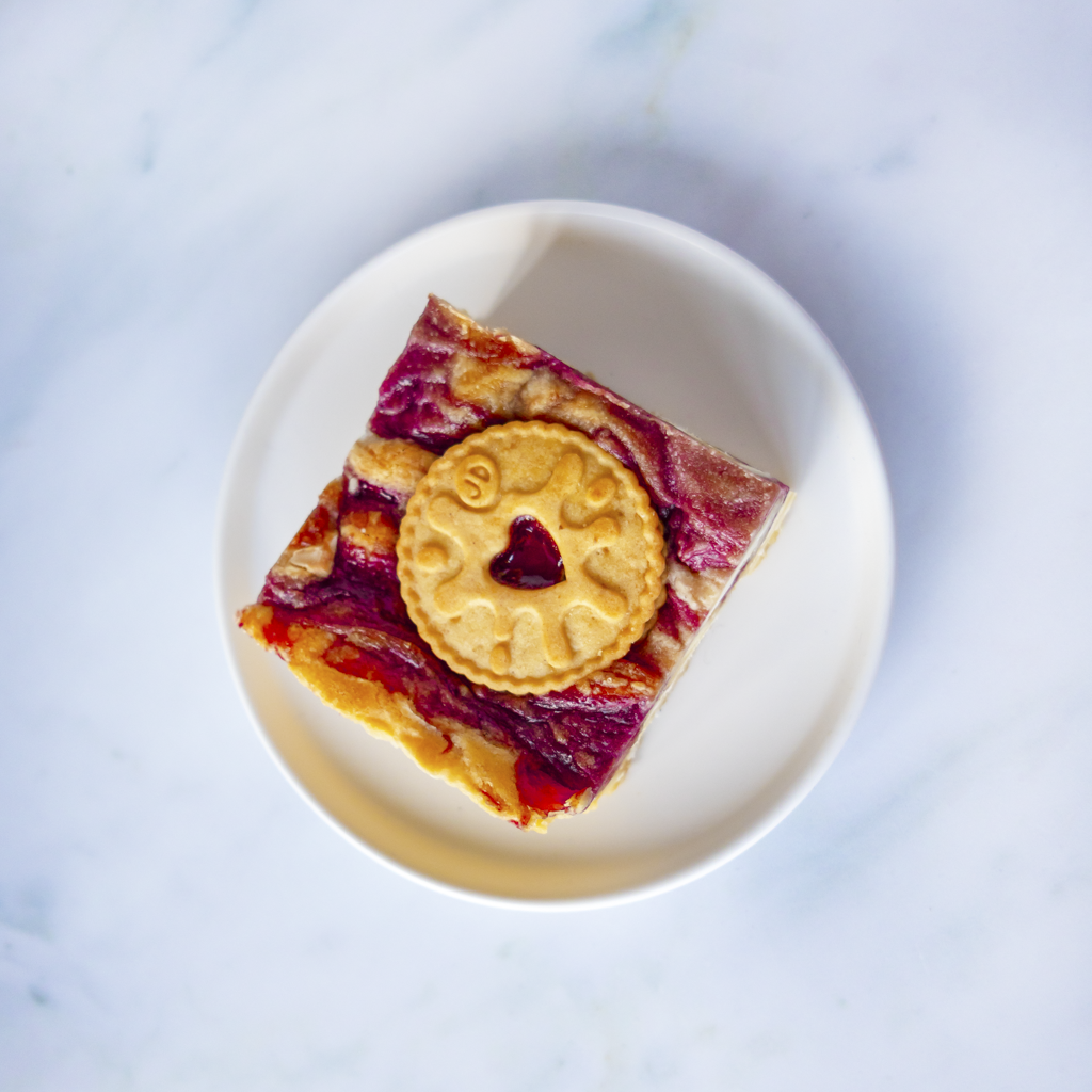 Square of layered dessert with a Jammie Dodger cookie on top, served on a white plate, ideal for Valentine gifts or sending to your lovers