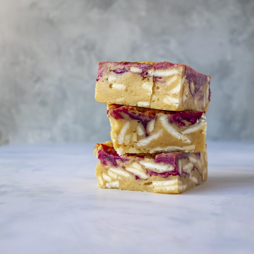 Stack of three Jammie Dodger Blondie Slab with a white chocolate and fruity marbled design on a marble surface.