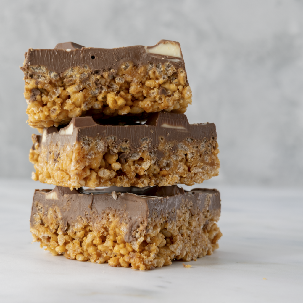 Three stacked Kinder Crispie Slab pieces with caramel rice crispy base and Kinder chocolate topping on neutral background