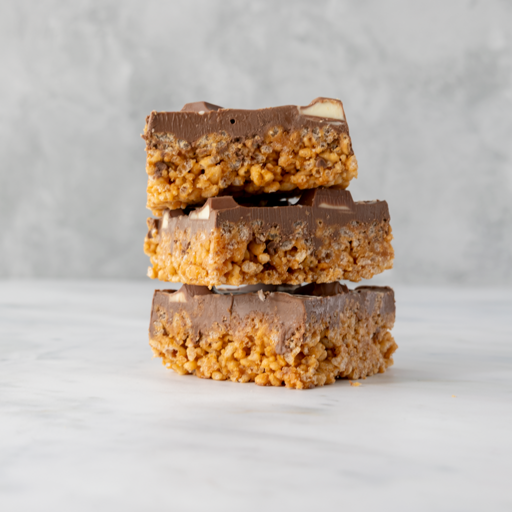 Three stacked Kinder Crispie Slab pieces with caramel rice crispy base and Kinder chocolate topping on neutral background