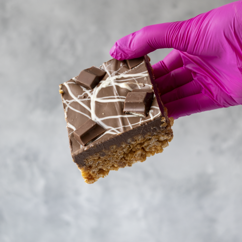 Kinder Crispie Slab held by a hand wearing a purple glove on a gray background