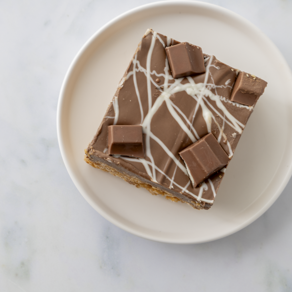Chocolate Kinder crispie slab slice served on white plate with white chocolate drizzle and Kinder chunks