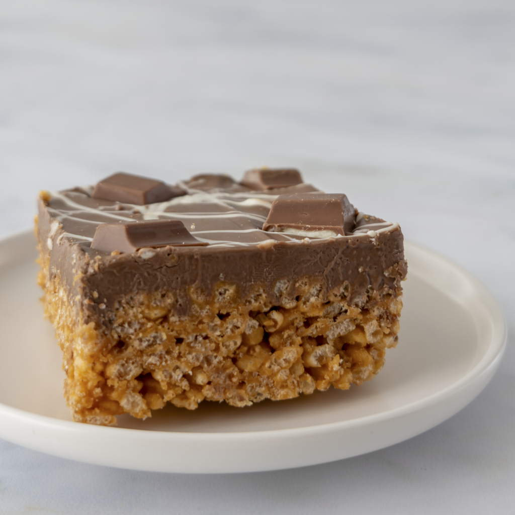ndulgent Kinder Crispie Slab on plate showing layered caramel crispie base and creamy chocolate topping