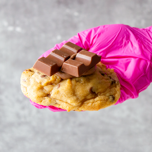 Kindertella Deluxe Cookie with chocolate pieces held by a pink glove on a gray background
