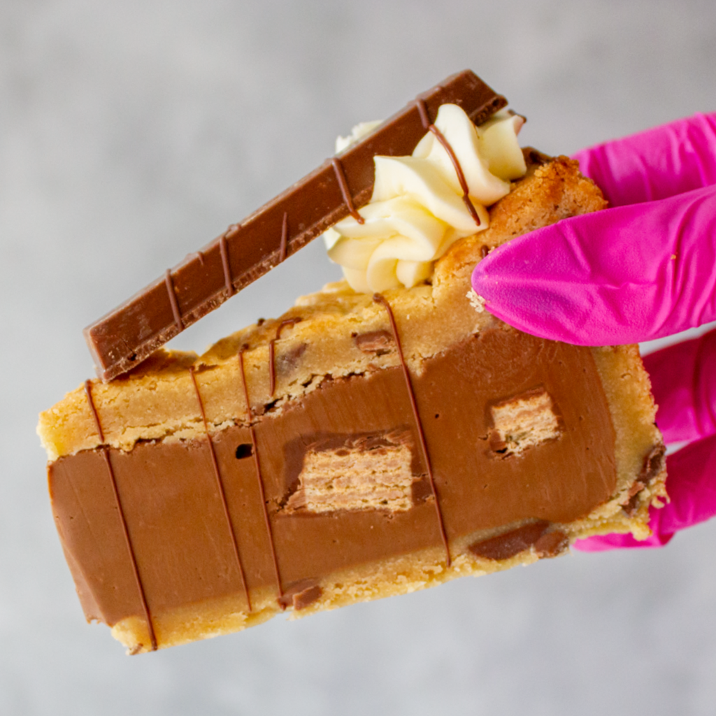 DoughGirl KitKat Crunch Cookie Pie with a pink gloved hand holding it against a gray background