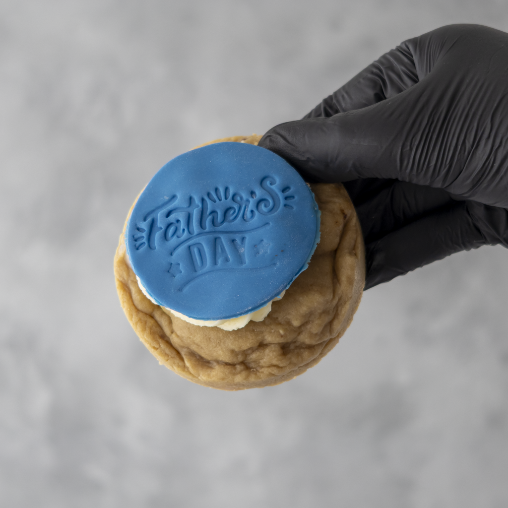 Cookie with 'Father's Day' stamp by DoughGirl UK held by a gloved hand against a gray background
