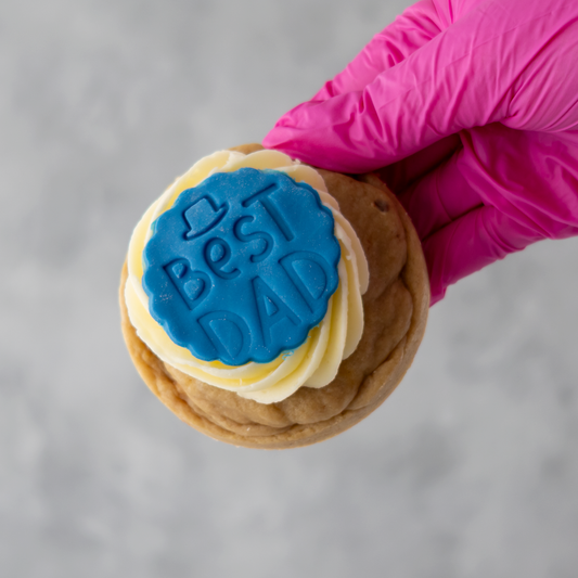 Father's day cookie with 'Best Dad' stamp held by a gloved hand against a gray background