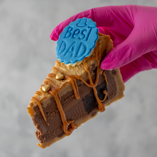 Father's Day Salted Caramel Brownie Cookie Pie Slice with 'Best Dad' decoration held by a gloved hand against a gray background