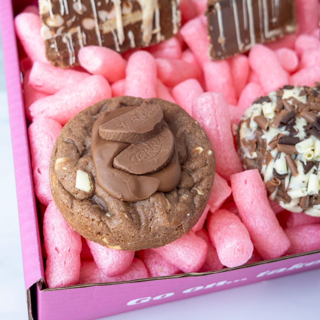 A close-up of a pink gift box featuring a chocolate cookie topped with Terry chocolate pieces and a triple chocolate cookie.
