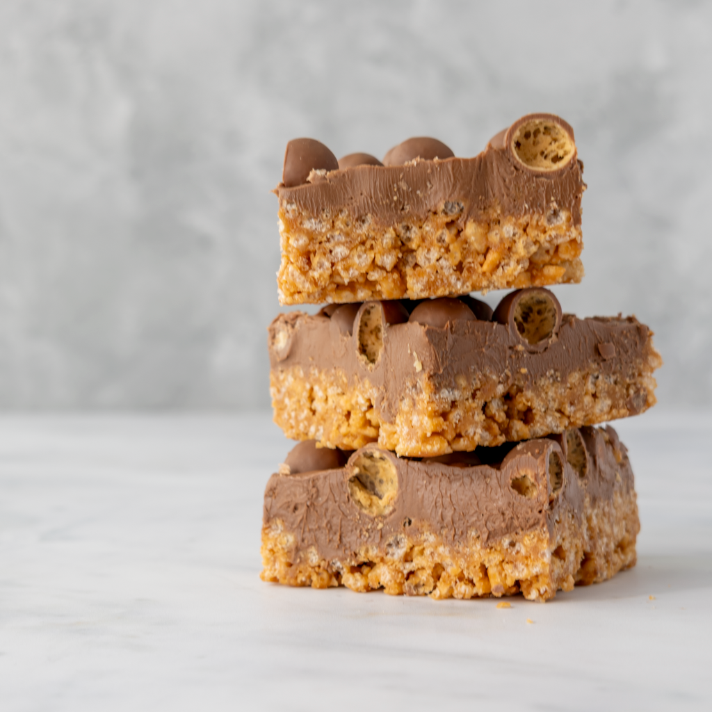 Three stacked Malteser crispie slab slices showing thick caramel rice crispie base and chocolate topping
