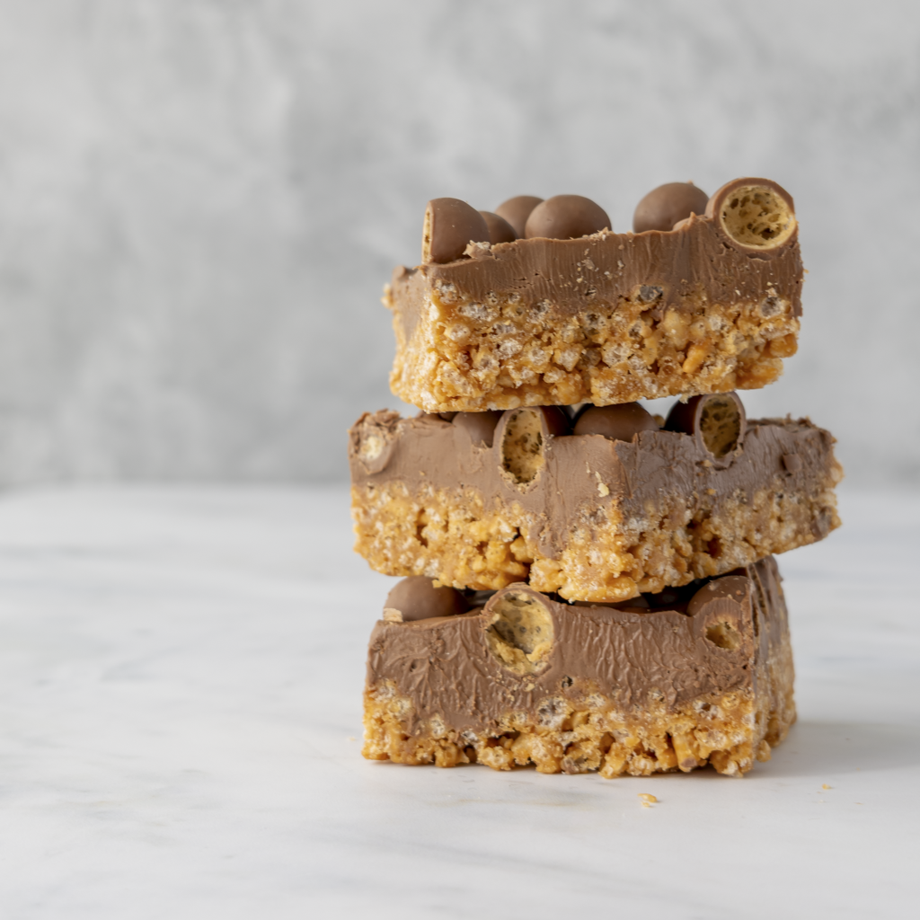 Three stacked Malteser crispie slab slices showing thick caramel rice crispie base and chocolate topping
