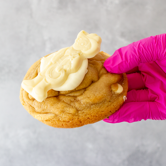Milkybar Deluxe Cookie with white frosting being held by a gloved hand on a gray background