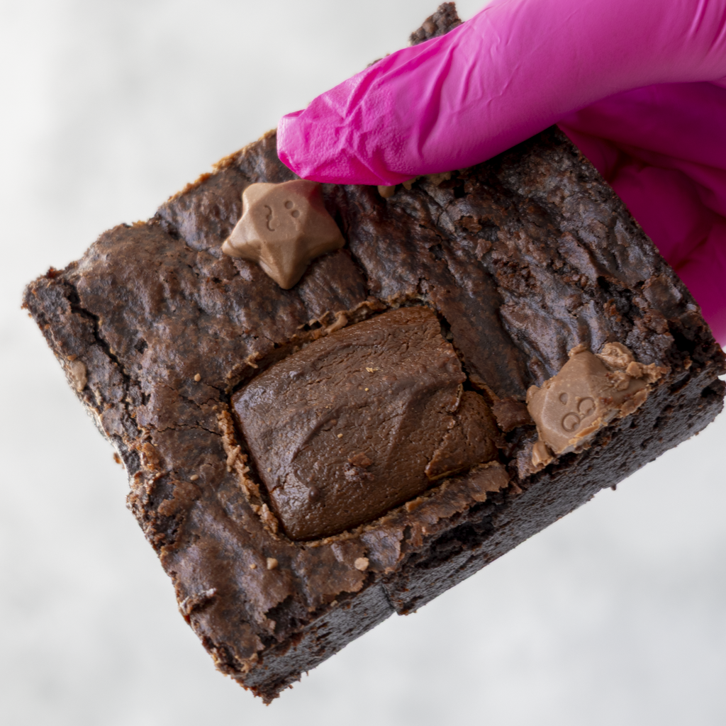 Milkyway Brownie Slab by DoughGirl UK with chocolate chips held by a gloved hand on a white background
