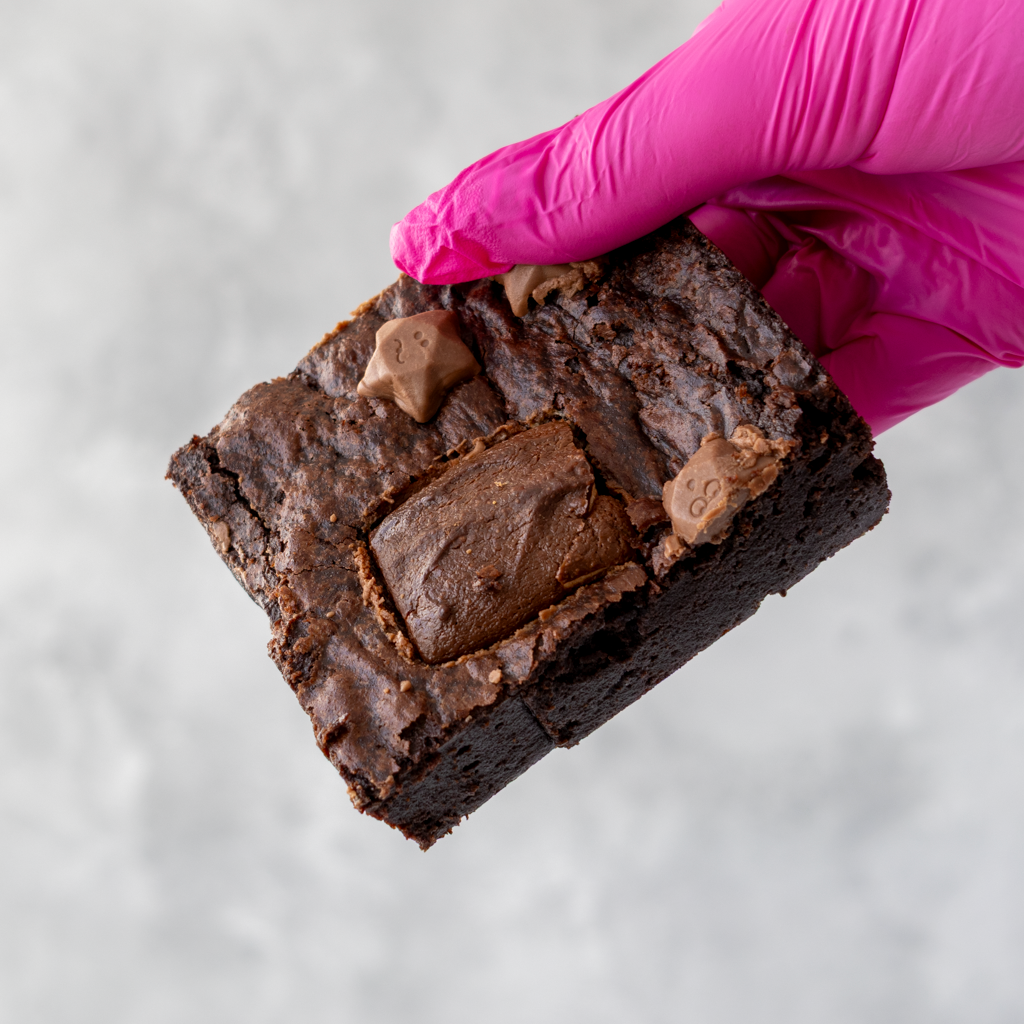 DoughGirl Milkyway Brownie Slab with Milkyway bar and Milkyway stars held by a hand wearing a pink glove on a light gray background