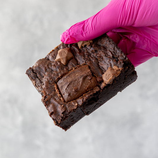 DoughGirl Milkyway Brownie Slab with Milkyway bar and Milkyway stars held by a hand wearing a pink glove on a light gray background