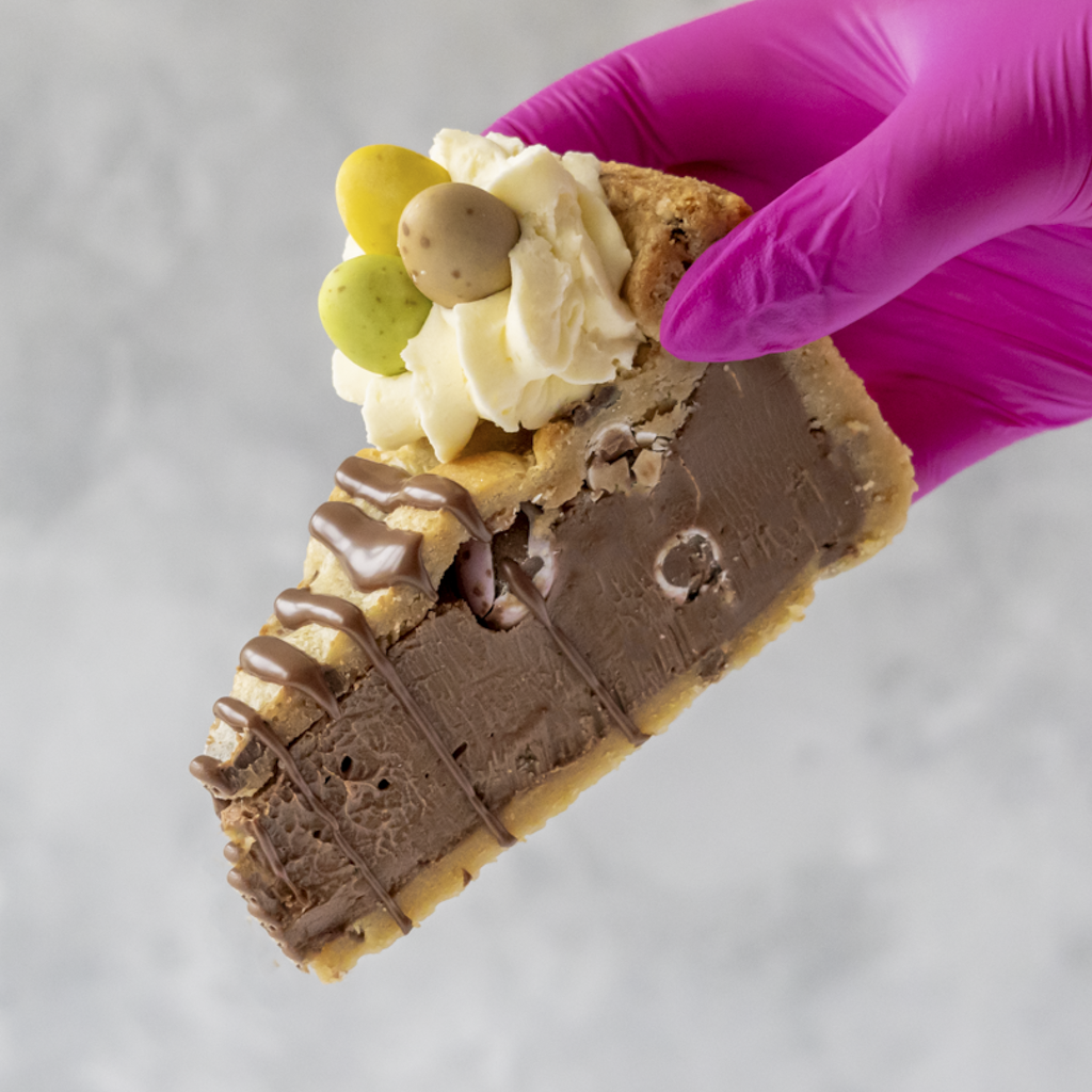 Limited Edition Malteser Bunny Cookie Pie Slice with chocolate drizzle and Mini Eggs held by a gloved hand.