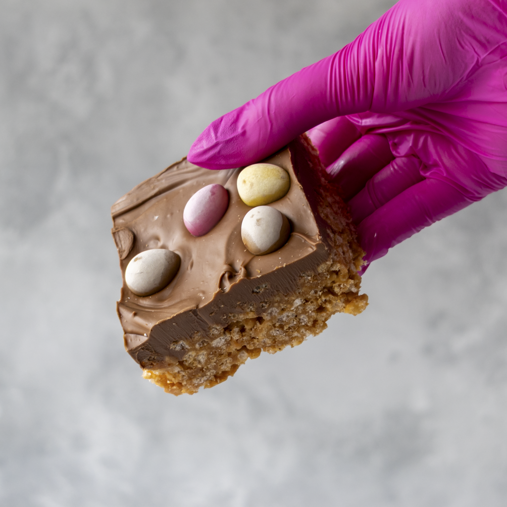 Mini Egg Crispie Slab held by a gloved hand on a neutral background