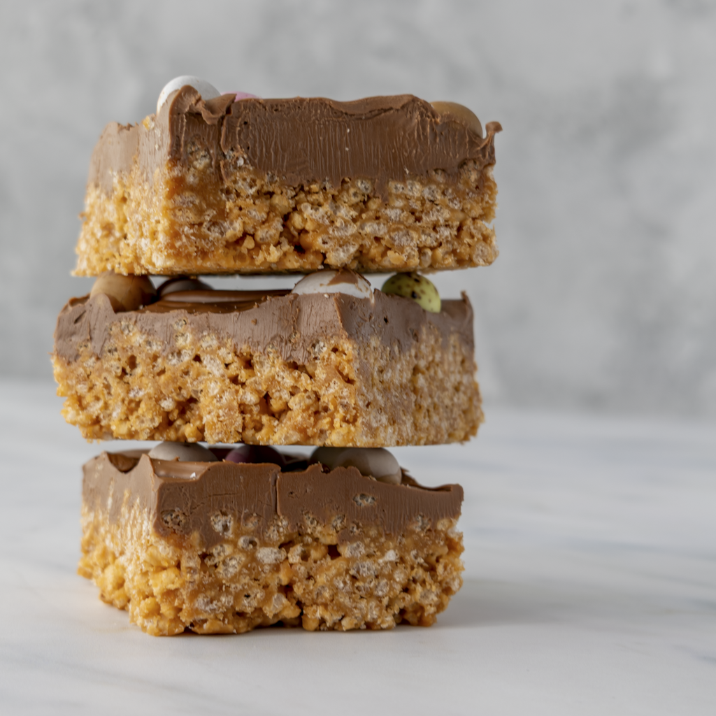 Close up 3 stacked Mini Egg Crispie Slab pieces highlighting caramel rice crispy base and chocolate mini egg topping