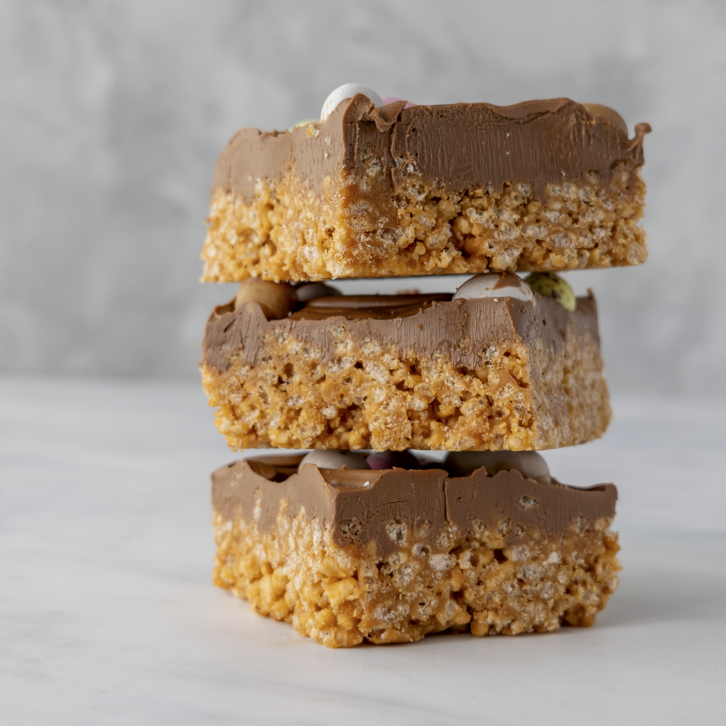 Chocolate crispie slab slices stacked to show thick caramel crispie base and mini egg topping
