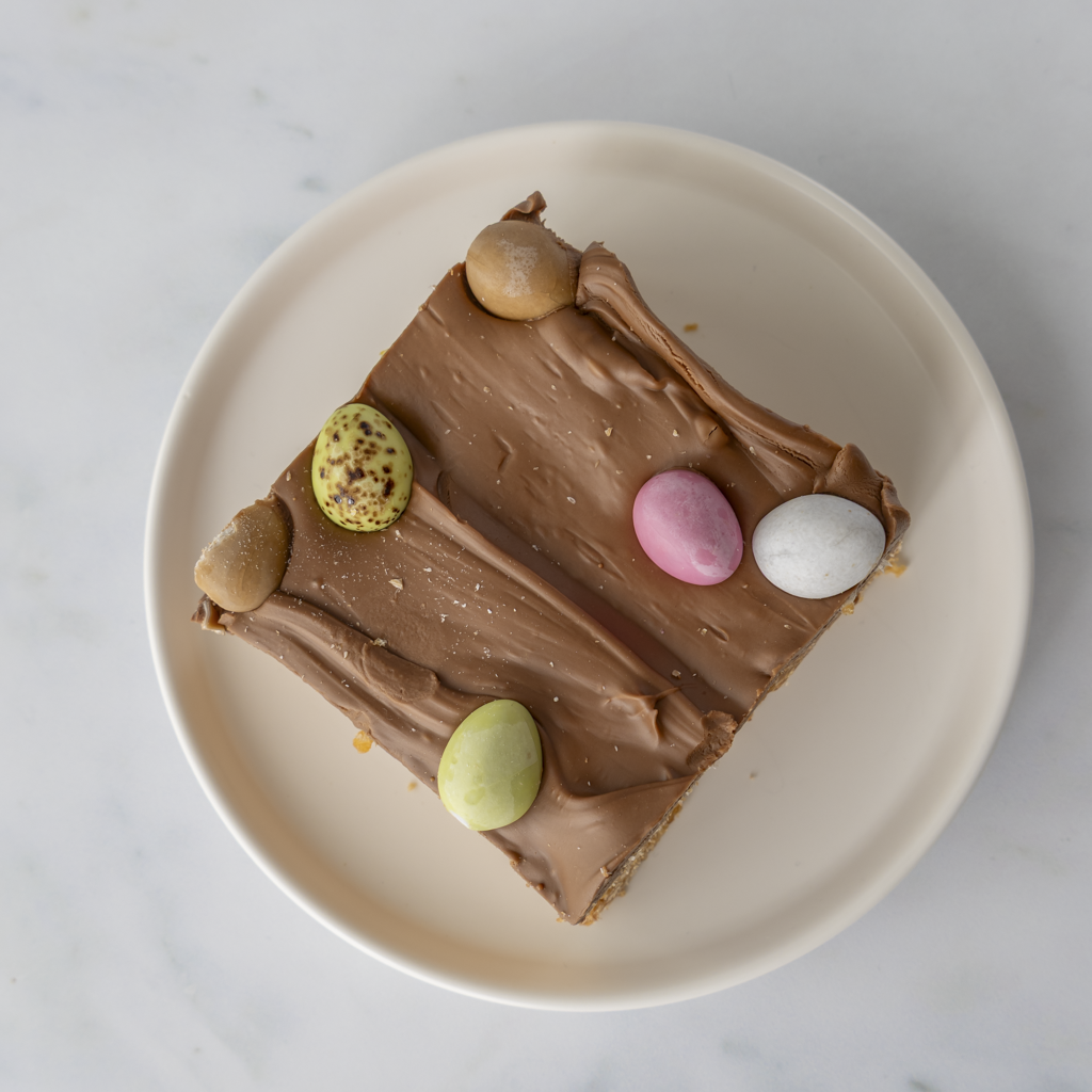 Mini Egg Crispie Slab dessert slice served on white plate with caramel rice crispy base and milk chocolate