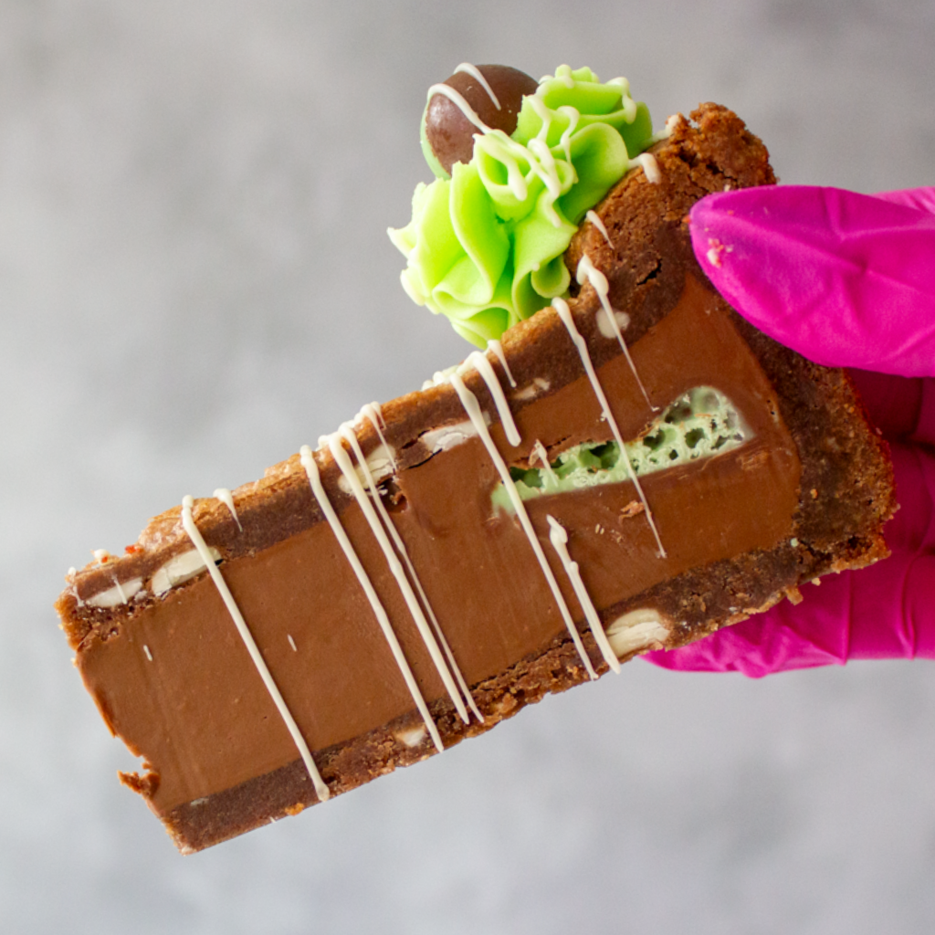 DoughGirl Mint Aero Cookie Pie with green frosting and a pink glove holding it against a gray background