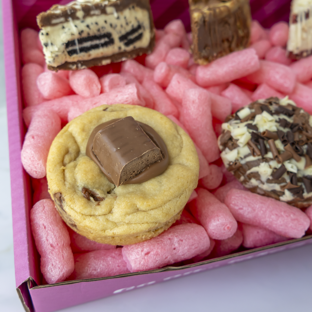 A close-up of assorted gourmet cookies and chocolate treats arranged in a pink box.