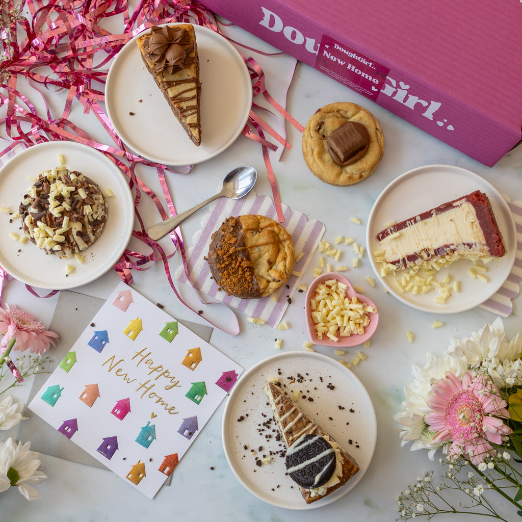 A styled flat-lay of assorted desserts and a pink box labeled 'DoughGirl New Home'.