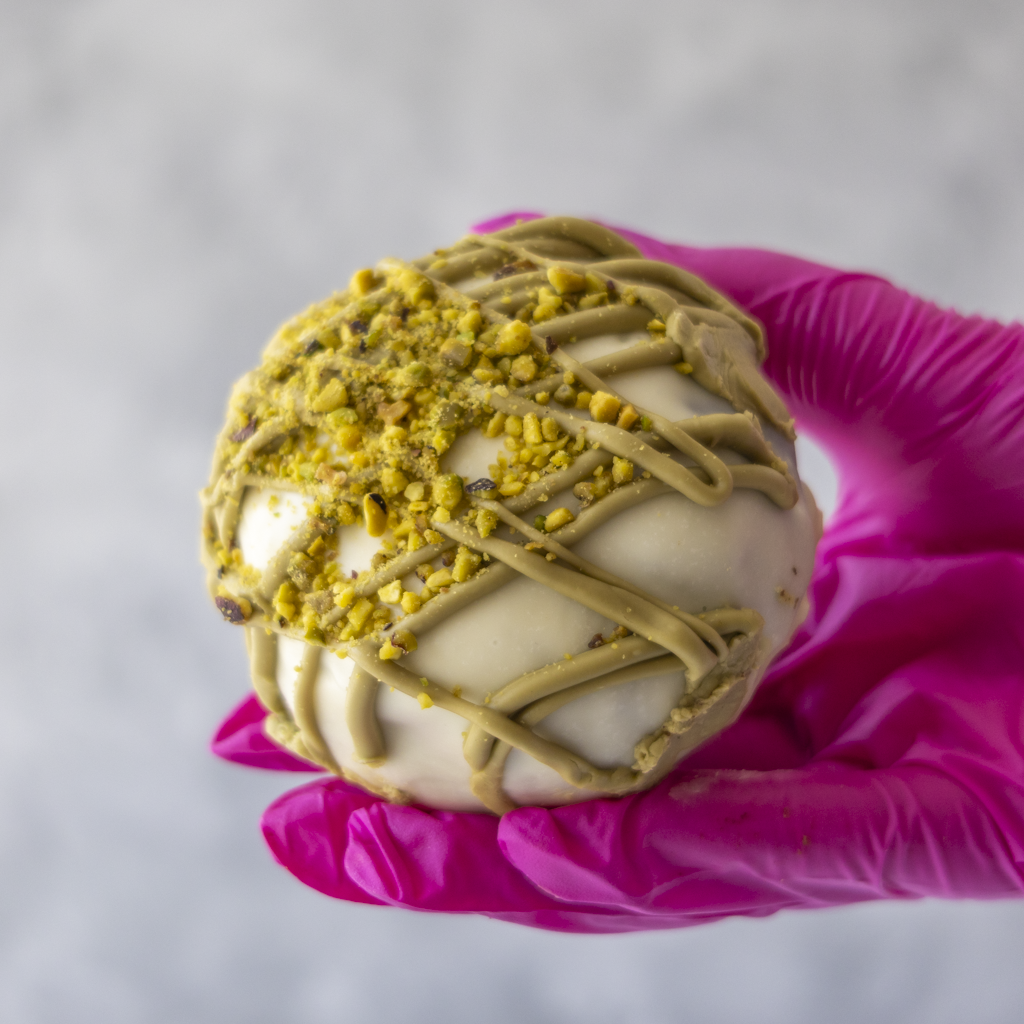 DoughGirl Pistachio Choccy Boom Bite held in pink glove with white chocolate and crushed pistachios